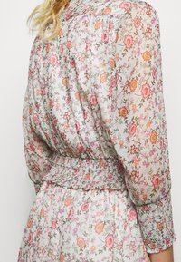 Sukienka w kwiaty wykonana z lekkiego, przejrzystego materiału, z marszczoną talią i bufkami na rękawach. Kolory obejmują róż, pomarańcz i zielone wzory.