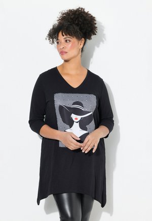 Schwarzes langärmliges Tunika mit V-Ausschnitt, das einen grafischen Druck einer Frau mit Hut und geometrischen Mustern zeigt. Glattes Material, asymmetrischer Saum.