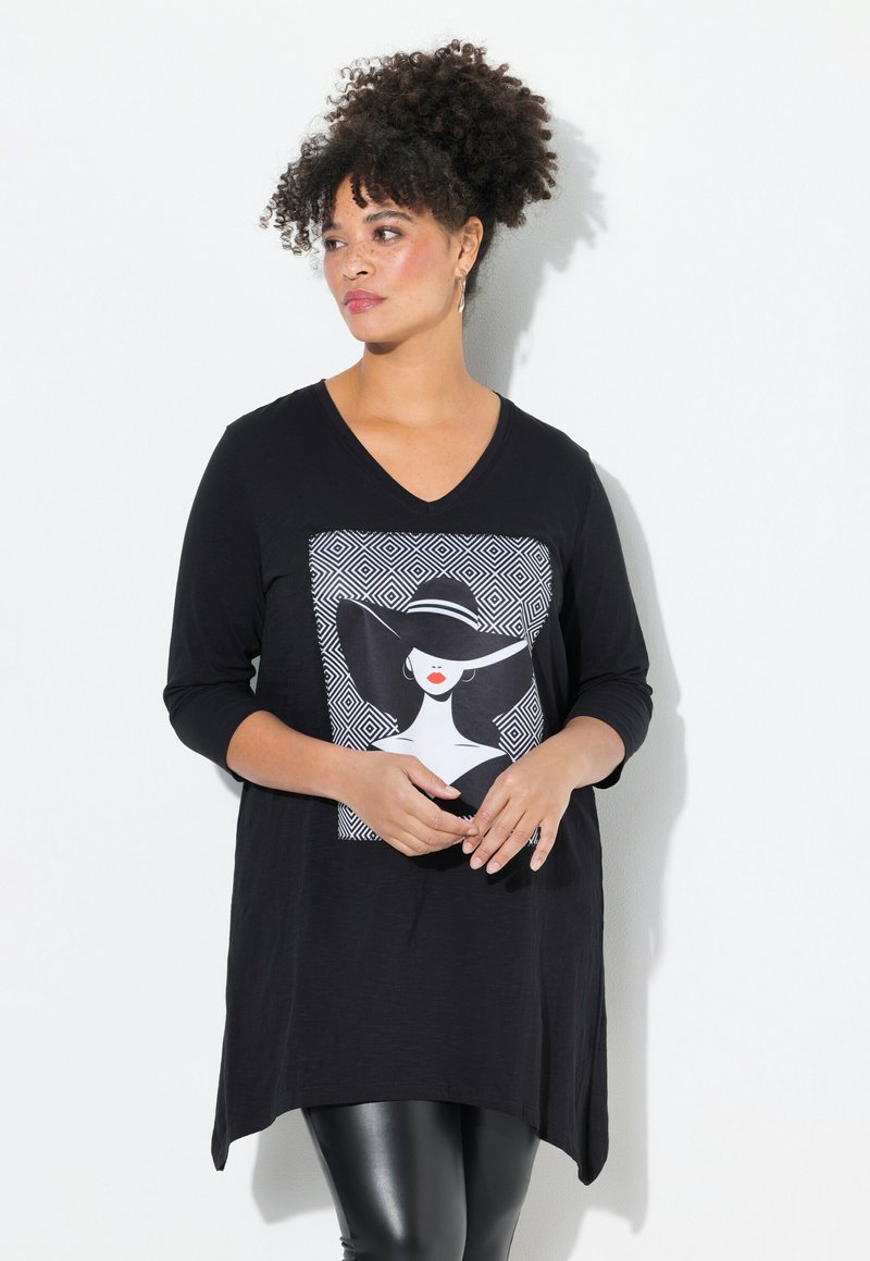 Tunic nera a maniche lunghe con scollo a V, caratterizzata da una stampa grafica di una donna con un cappello e motivi geometrici. Tessuto morbido, orlo asimmetrico.