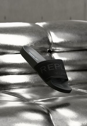 Čierna šľapka na nohu so štruktúrovaným remienkom s vystupujúcim logom "REPLAY". Elegantný, minimalistický dizajn, umiestnený na lesklej striebornej ploche.