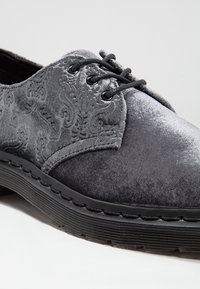 Chaussure gris en velours à lacets avec un motif floral en relief sur les côtés et une semelle épaisse en caoutchouc noir.