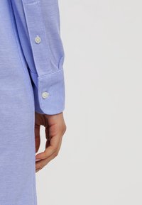 Helles blaues Hemd mit strukturiertem Muster, langen Ärmeln und weißen Knöpfen an den Bündchen. Der Stoff wirkt atmungsaktiv und weich.