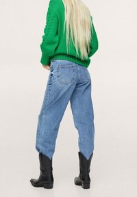 Groene gebreide trui met een oversized pasvorm, lichtblauwe hoge taille jeans met een relaxte uitstraling, en zwarte kniehoge laarzen.