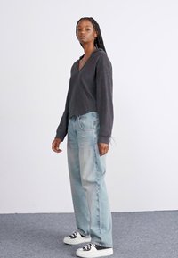 Un hoodie oversize gris avec un col en V, associé à un jean baggy bleu clair. La tenue est complétée par des baskets noir et blanc.