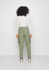 Green fleece joggers with side cargo pockets, elastic waistband, and ribbed cuffs, paired with a white long-sleeve top and sneakers.