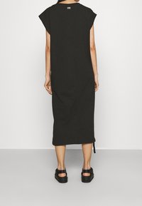 Czarna bawełniana sukienka t-shirtowa z krótkimi rękawami, długim prostym krojem i bocznymi rozcięciami, z małą metką na tyle dekoltu.