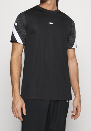 Homme portant un maillot de sport noir avec des manches à motifs foncés et des logos Nike swoosh blancs sur les manches et le pantalon.