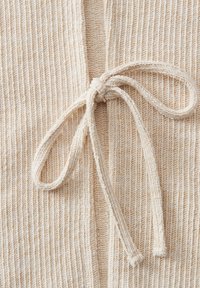 Close-up van beige gebreide stof met een gestrikte strik gemaakt van hetzelfde geribbelde breimateriaal.