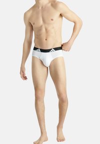 Weiße Herrenboxershorts mit einem schwarzen elastischen Bund, der drei weiße Streifen aufweist. Der Stoff wirkt glatt und enganliegend.