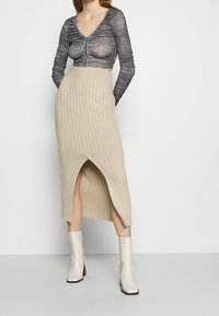 Beige Rippstrickrock mit hohem Schlitz und taillierter Taille, kombiniert mit einem strukturierten grauen Cropped-Top und weißen Knöchelstiefeln.