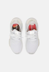 Vita gymnastikskor med ett mesh-övre, rund tå, tjocka vita snören och en strukturerad sula. Logotyper synliga på tungan och innersulan.