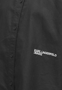 Camisa negra de botones, hecha de un tejido suave, con el logotipo bordado en blanco "KARL LAGERFELD JEANS" en el lado izquierdo.