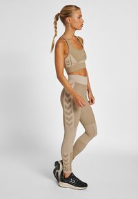 Beige sport-bh och hög midja leggings med ett texturerat mönster och pilaccenter. Kombinerat med svarta träningsskor.