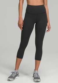 Zwarte hoge taille capri leggings van rekbaar materiaal, met een gladde afwerking en een enkel-lengte ontwerp, gecombineerd met grijze sportschoenen.