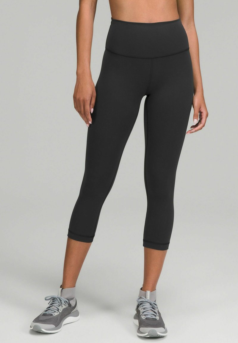 Zwarte hoge taille capri leggings van rekbaar materiaal, met een gladde afwerking en een enkel-lengte ontwerp, gecombineerd met grijze sportschoenen.