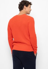 Oranssi röyhelöneule, jossa on pyöreä kaula-aukko ja pitkät hihat, ja joka sisältää tiukat vyötärönauhat ja teksturoitua kangasta. Yhdistetty tummiin housuihin.