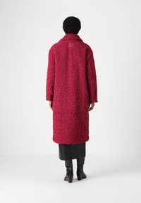 Abrigo largo y texturizado en un profundo magenta, hecho de una tela suave y esponjosa, con cuello y mangas largas, que llega a la mitad de la pantorrilla.