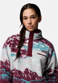 Sudadera de forro polar con cuello alto, patrón de montañas en color burdeos, azul claro y blanco, con botones de presión y un pequeño bolsillo en el pecho.