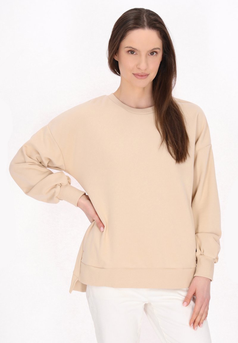 Beige mikina s kulatým výstřihem, dlouhými nabíranými rukávy a žebrovanými manžetami. Má volný střih a postranní rozparky na lemu. Měkká textura.