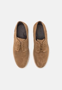 Scarpe da dress in suede marrone con punta rotonda, design con lacci, dettagli di cucitura discreti e superficie texture. Logo del brand visibile all'interno.