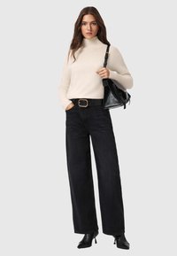 Beżowy sweter z golfem, czarne spodnie z wysokim stanem w szerokim kroju, czarny pasek z złotą klamrą oraz czarna torebka. Całość dopełniają botki na obcasie.