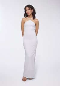 Abito maxi bianco a coste con una silhouette aderente, caratterizzato da un collo a halter e uno spacco laterale, abbinato a sandali con cinturini.