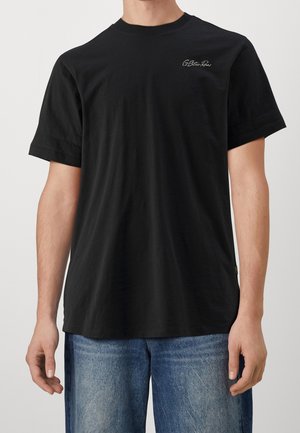 Camiseta de algodón negra con mangas cortas, escote redondo y un sutil logo bordado en el pecho. Diseño ligero y casual.