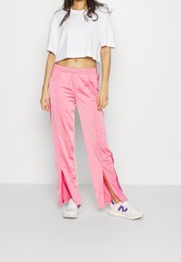 Pink track pants with side slits, elastic waistband, and contrasting purple stripes. Paired with a white cropped T-shirt and sneakers.