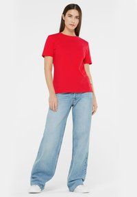 Red cotton t-shirt with short sleeves, crew neck, and a fitted shape, paired with light blue wide-leg jeans and white sneakers.