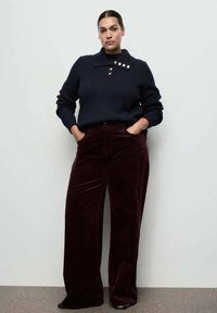 Suéter de punto azul marino con cuello abotonado, combinado con pantalones de pana burdeos de pierna ancha. Textura suave y corte relajado.