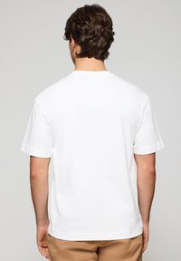 Biała koszulka z bawełny, z klasycznym okrągłym dekoltem, krótkimi rękawami i luźnym krojem. Gładka faktura, prosty design, brak widocznych wzorów lub grafik.