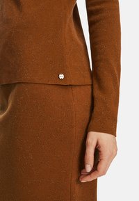 Brauner Strickpullover und Rock-Set mit feinem Muster, metallischen Akzenten und kleinem Markenlogo am Saum.