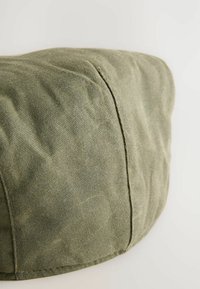 Grüne Stoffmütze mit einer weichen, strukturierten Oberfläche, die ein schlankes Design und sichtbare Nähte entlang der Säume aufweist.