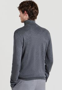 Grauer, gestrickter Rollkragenpullover mit schlanker Passform und gerippten Akzenten am Kragen und Saum. Das Material wirkt weich und strukturiert.