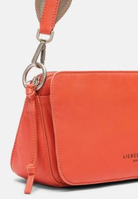 Borsa a tracolla in pelle corallo con una texture liscia, design piatto e hardware in argento. Cintura regolabile con un accento in tessuto intrecciato.