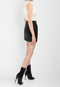 Biała ribbed bezrękawnik połączony z czarną mini spódnicą z wysokim stanem z skóry. Czarne botki do kostki z lakierowanej skóry dopełniają outfit.