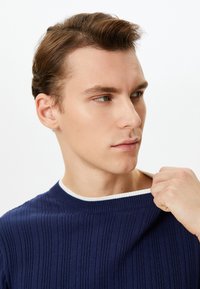 Granatowy sweter w prążki z białym akcentem na dekolcie. Materiał wydaje się miękki, a luźny krój ma subtelne detale tekstury.