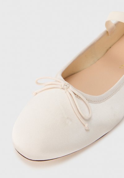 Μπεζ μπαλαρίνες με μαλακό υφασμάτινο πάνω μέρος, στρογγυλή μύτη, ελαστικό λουράκι στον αστράγαλο και διακοσμητικό φιόγκο στο μπροστινό μέρος. Ομαλή υφή και στρογγυλεμένο σχήμα.