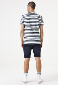 Camiseta de rayas en azul claro y marino, combinada con pantalones cortos oscuros y enrollados. El modelo lleva zapatillas blancas con calcetines a rayas azules.