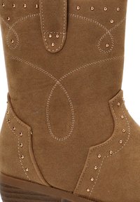 Botín de ante marrón con costuras decorativas y tachuelas de cobre, que presenta una punta redonda y un tacón bajo apilado para mayor estabilidad.
