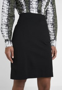 Černá úzká sukně z elastického materiálu, délky po kolena, s hladkým povrchem a čistými liniemi, v kombinaci se vzorovanou košilí s dlouhým rukávem.