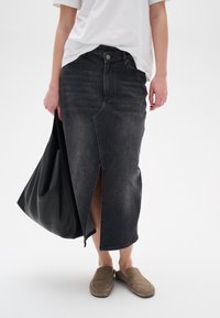 Black denim skirt with a front slit, high waist, and contrasting stitching, paired with a loose white t-shirt and brown slip-on shoes.