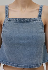 Modra denim crop majica z širokimi naramnicami, kvadratnim izrezom in sproščenim krojem. Tkanina ima gladko teksturo in je zaključena z raztrganim robom.