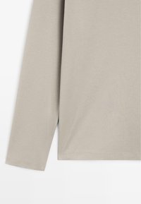 Top met lange mouwen in licht taupekleurige stof. Heeft een gladde textuur en een eenvoudig ontwerp, met een rechte zoom en aansprekende manchetten.