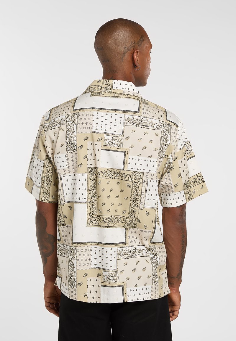 Chemise à manches courtes en tissu léger, présentant un motif patchwork beige et blanc avec des accents noirs et des graphiques détaillés.