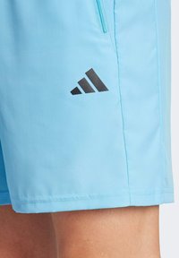 Svijetloplave atletske šorceve od mekog materijala, s crnim Adidas logotipom sa strane i džepom s patentnim zatvaračem za pohranu.