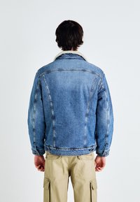Ljusblå denimjacka med en sherpa-fodrad krage, med en avslappnad passform, strukturerade sömmar och knappdetaljer vid ärmslutet.