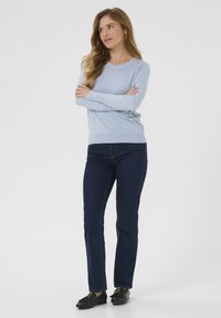 Pull léger bleu à manches longues associé à un jean slim bleu foncé et des mocassins noirs. Le pull présente un col rond et une texture lisse.
