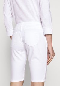 Pantalones cortos de mezclilla blanca con una cintura de altura media, diseño de cinco bolsillos y puños doblados. Textura suave con detalles de costura sutiles.