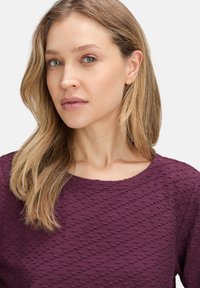 Haut texturé violet avec un col rond, présentant un motif subtil et des manches courtes, mettant en avant un tissu doux et respirant.